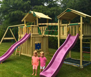 Aire de jeux en bois avec deux toboggans, filet à grimper, pont de singe et balançoires dans un jardin